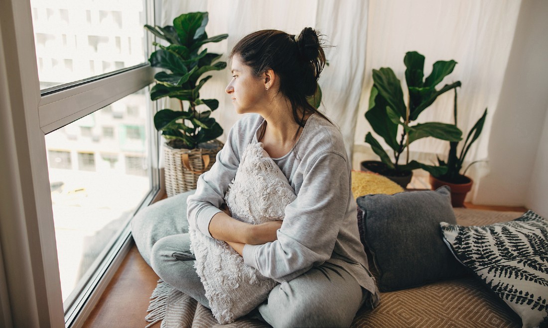 woman sitting in front of window looking outside sad coronavirus