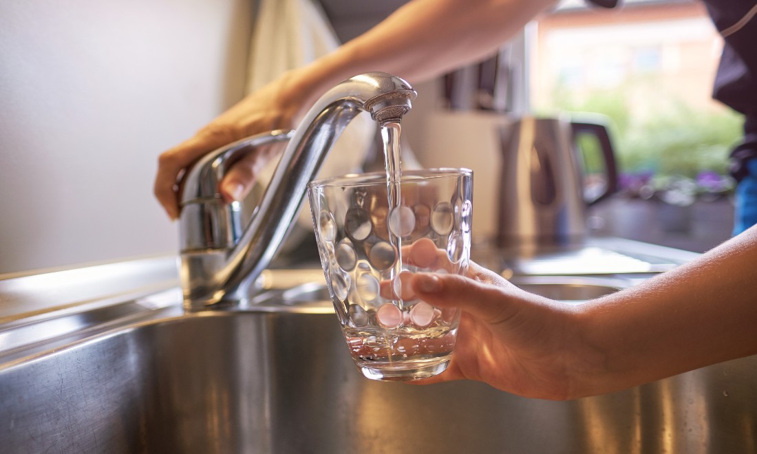 A parent and child filling a glass of water at a kitchen tap