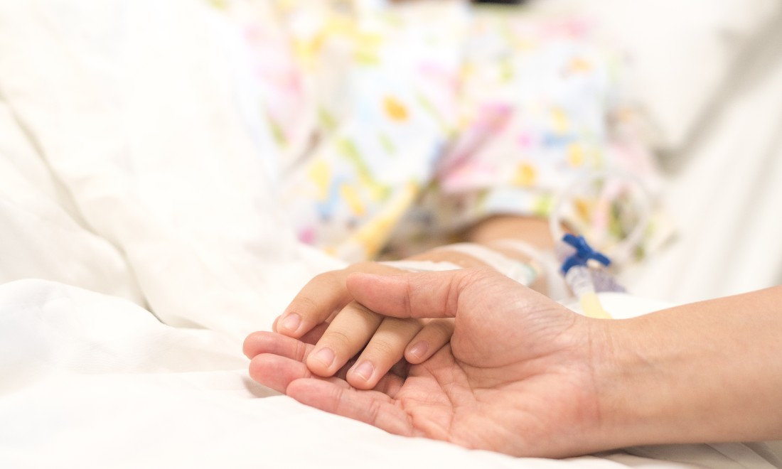 Parent holding the hand of a sick child lying in hospital