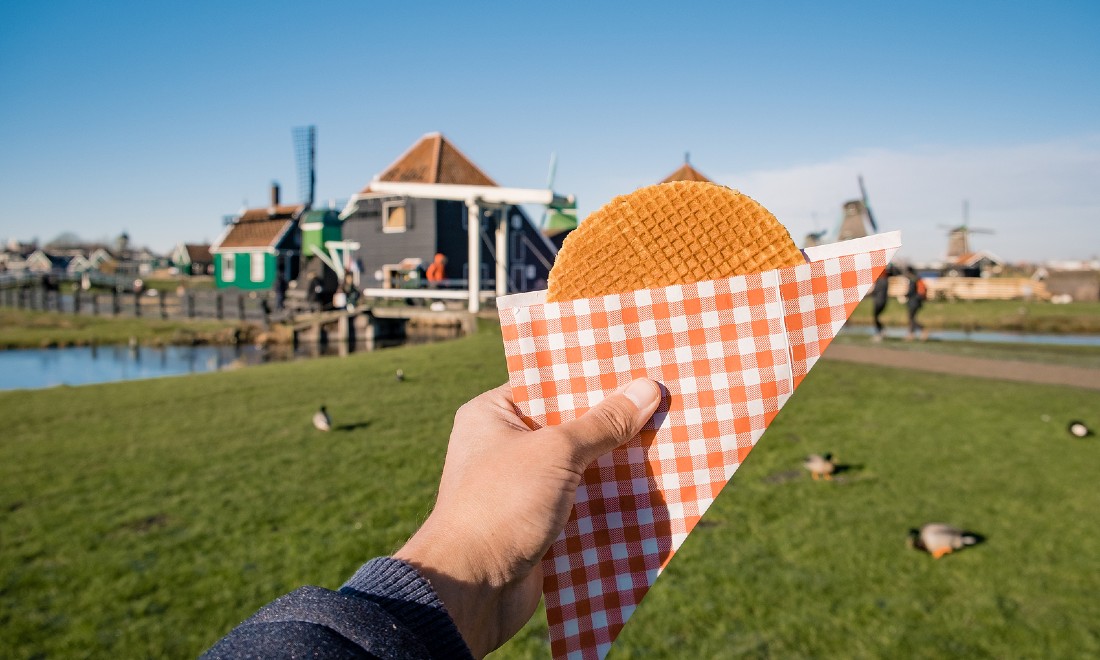 someone holding up stroopwafel, zaanse schans in background