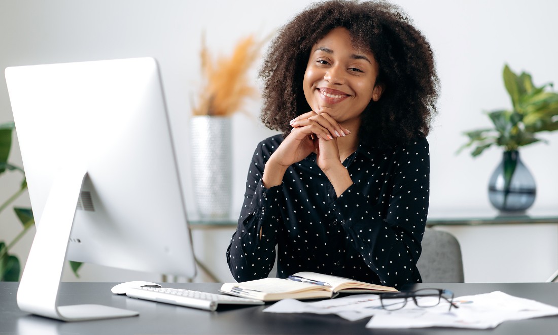 Woman smiling behind laptop at work - Get that promotion; don't make these mistakes!