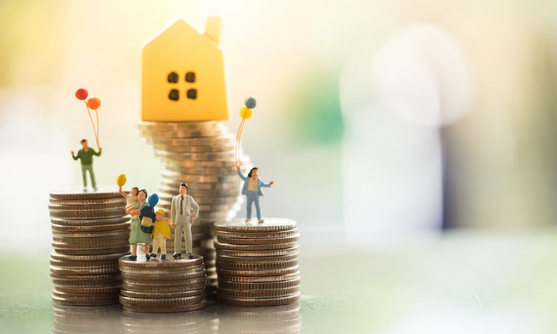 Family figures standing on coins near model house