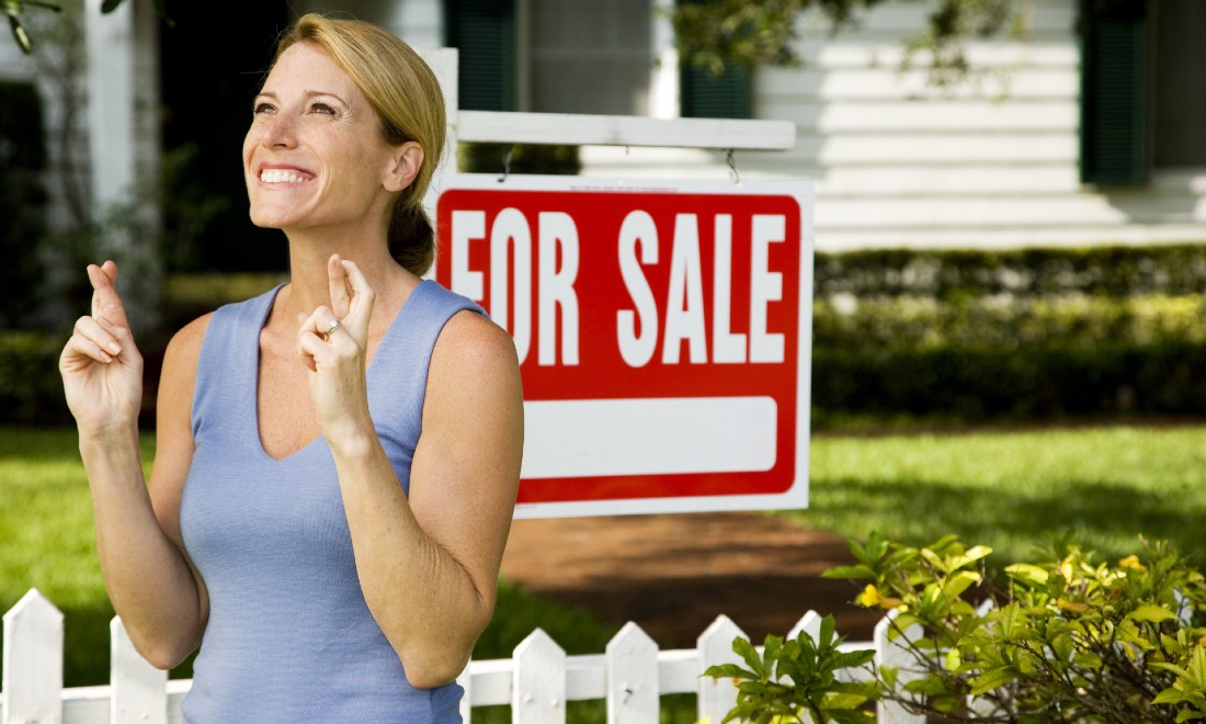 woman with fingers crossed in front of home that's for sale