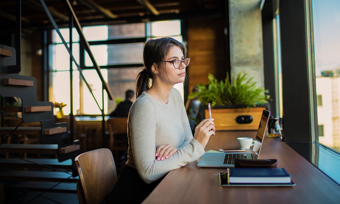 woman on laptop, looking out window pensively