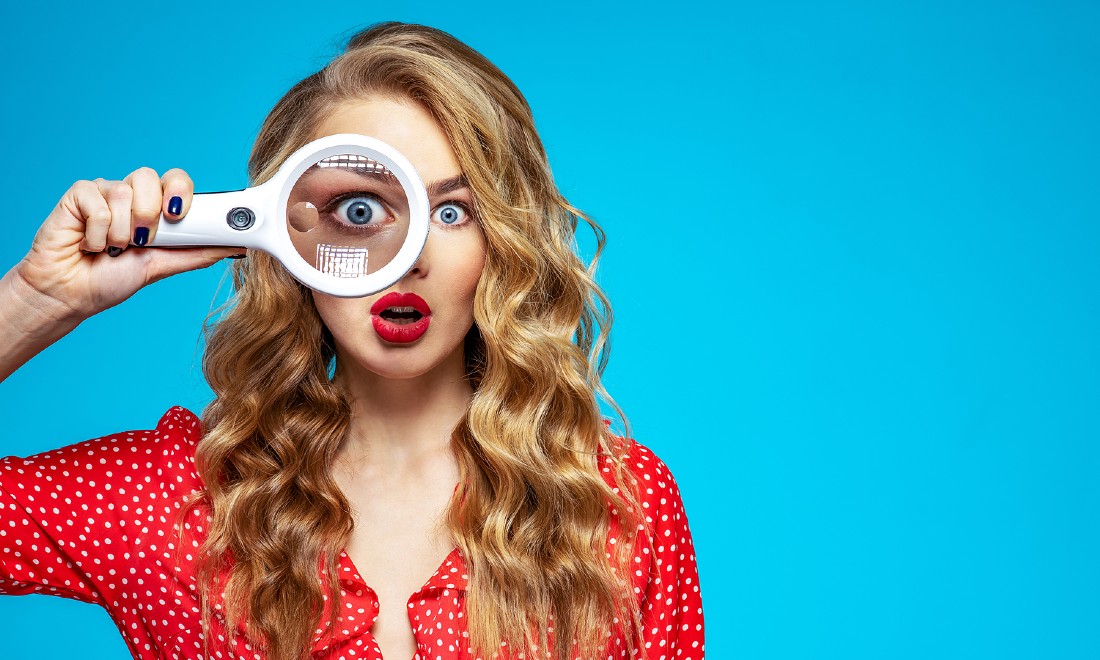 woman holding up magnifying glass, bright blue background