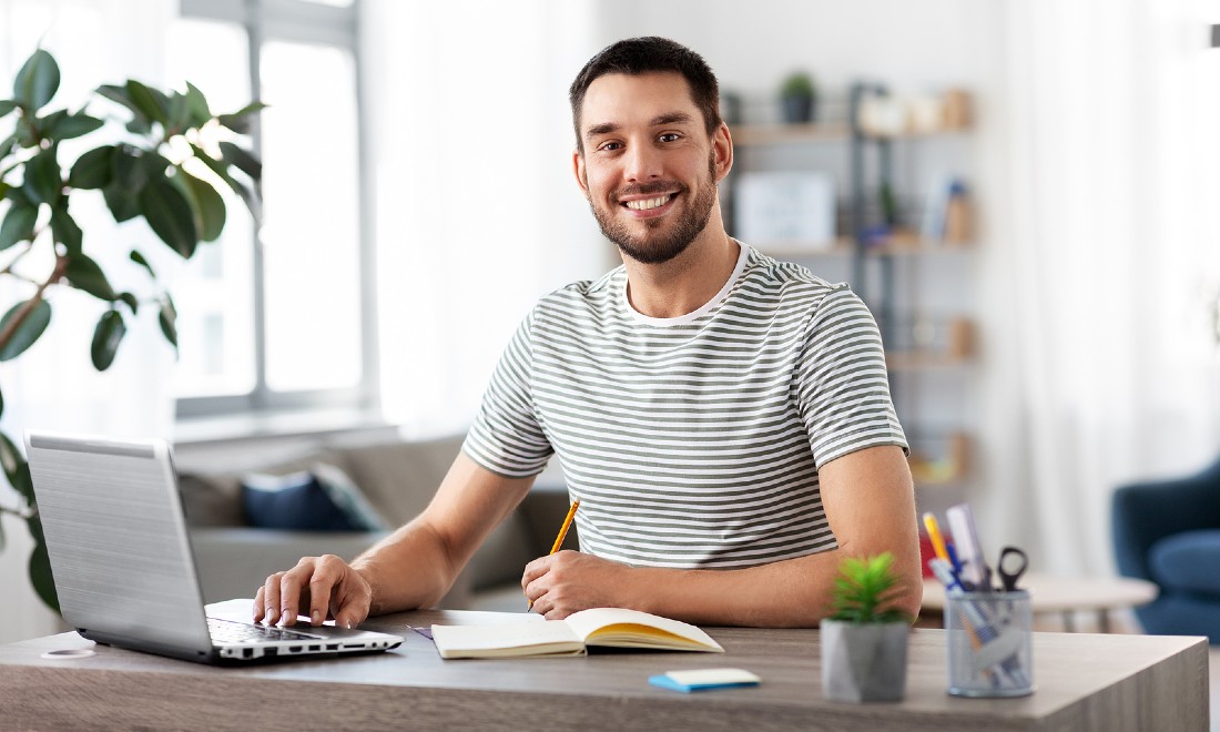 man behind desk on laptop with notebook