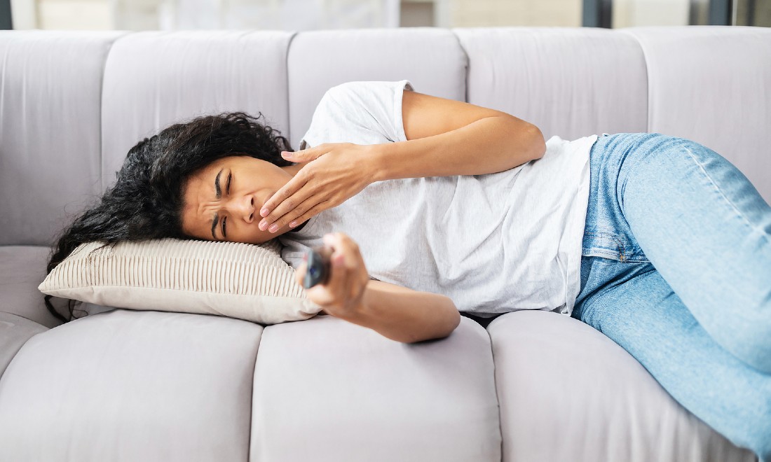 woman lying on couch, yawning, watching tv