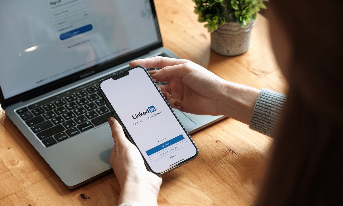 Woman logging into LinkedIn on mobile, laptop