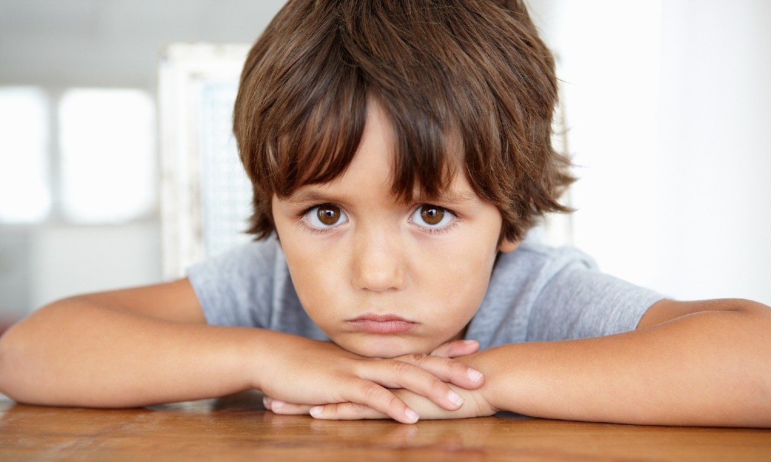 sad, mad child looking into camera, leaning on table