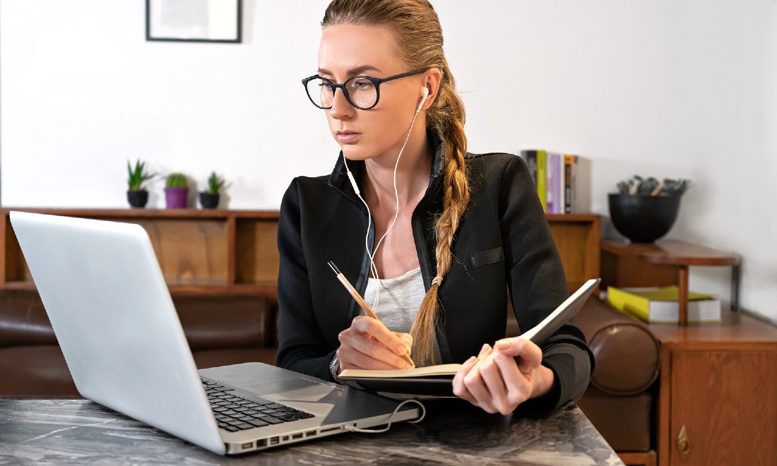 woman working on laptop writing notes in notebook