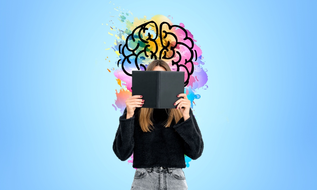 Woman reading a book in front of colourful brain image - Want to keep your brain performing at its peak? Learn a language! by Regina Coeli