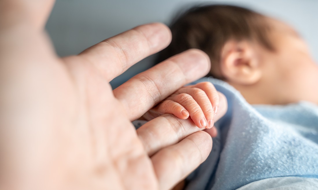 Parent holds the hand of their newborn baby