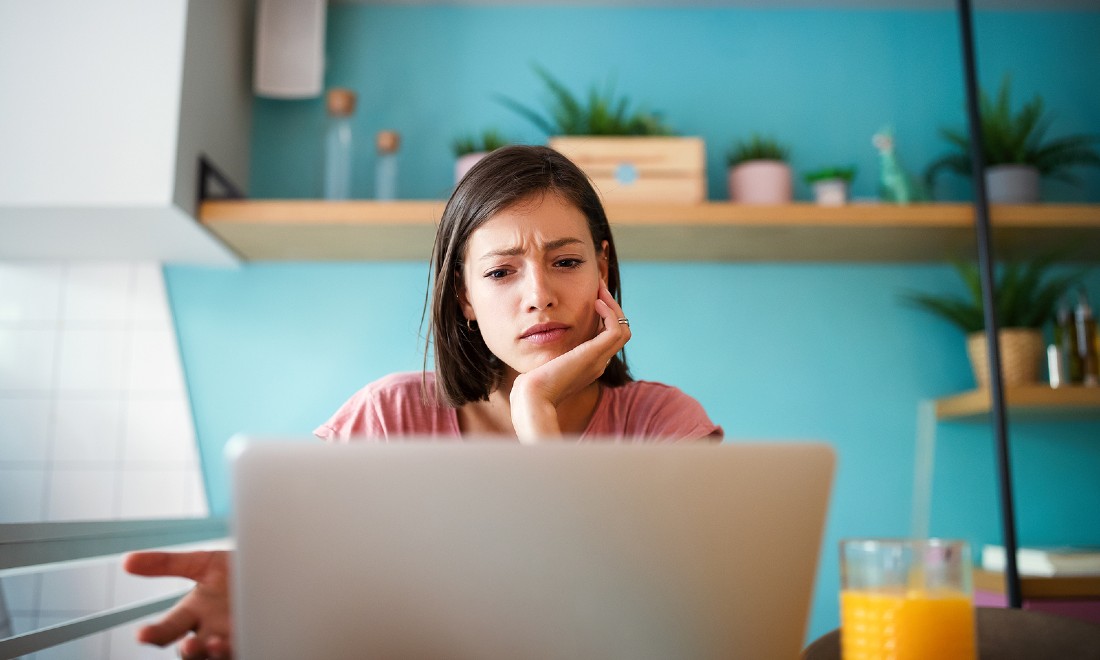 woman behind laptop in kitchen looking stressed