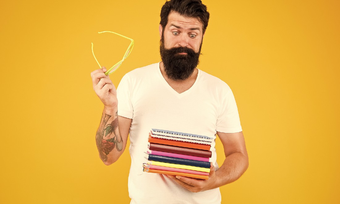 hipster man holding stack of books looking scared