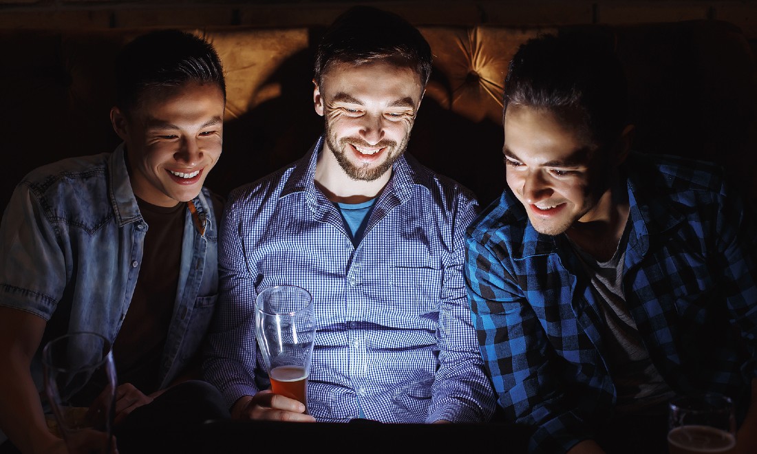 three young men using laptop holding beer