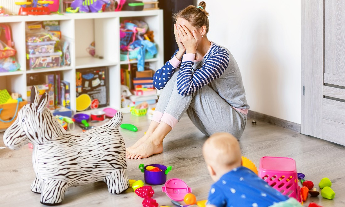 mother sitting on floor between toys, hands in front of face, tired