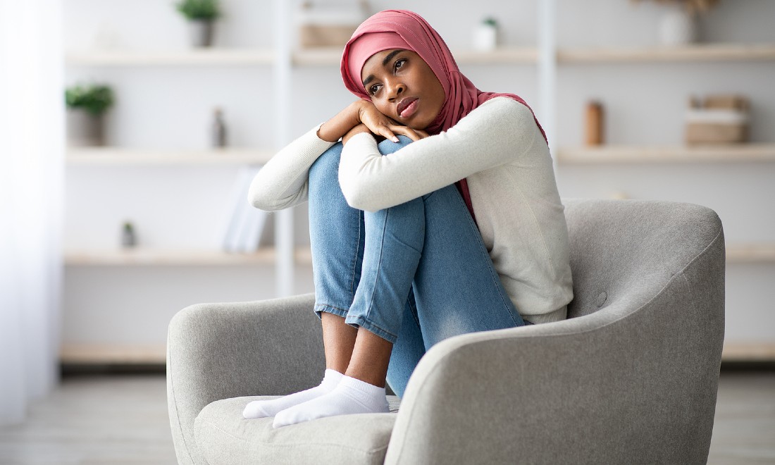 Woman sitting on chair, feeling lonely, arms wrapped around legs