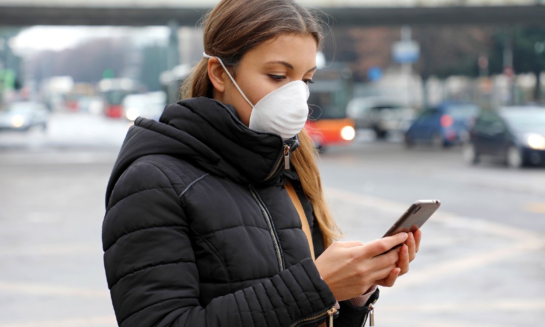 young woman wearing surgical mask on phone outside